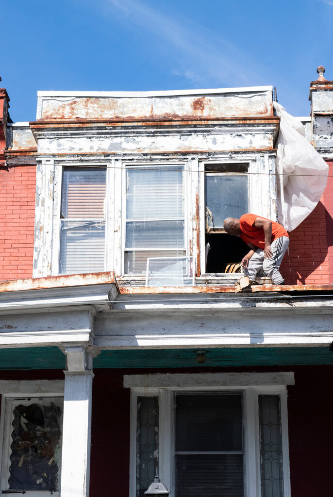 A man standing on a rooftop as he looks inside a house.