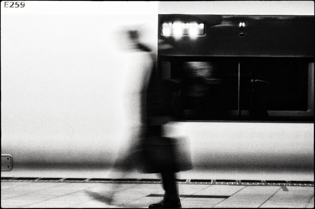 A Black and white image of a man walking down the street with a motion blur effect