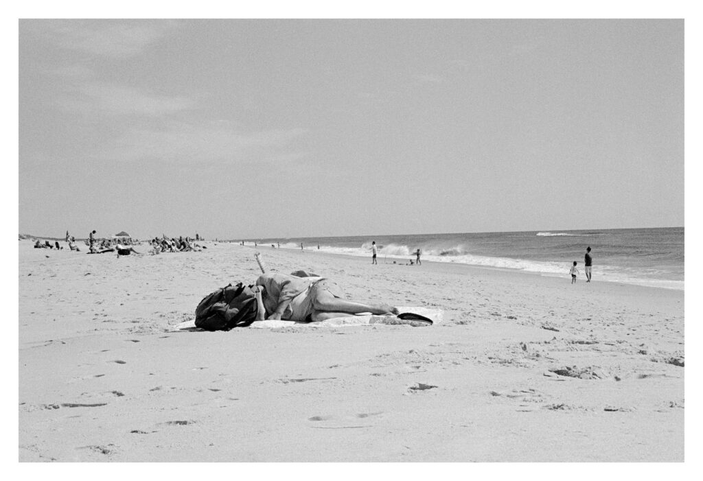 Black and white photography, a bather lies on the sand.